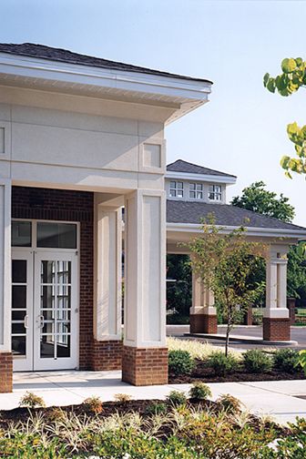 A modern building entrance featuring brickwork and columns surrounded by a landscaped courtyard.