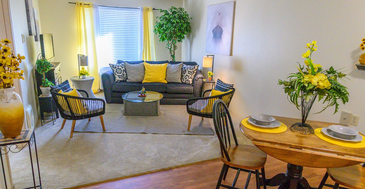 A cozy living room with a modern grey sofa and yellow accents, featuring armchairs and a central coffee table.