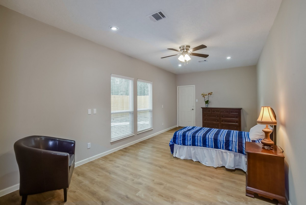 A spacious bedroom with wood flooring and a ceiling fan, featuring natural light from large windows.