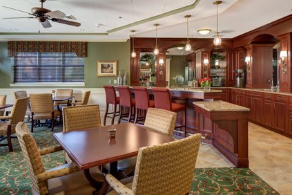 A cozy dining area with a bar, featuring tables and chairs, warm lighting, and a ceiling fan.