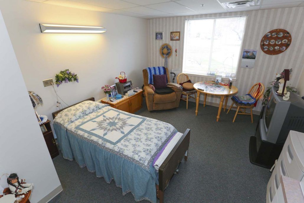 A cozy bedroom with a single bed, a small table set, and armchairs, illuminated by a large window.