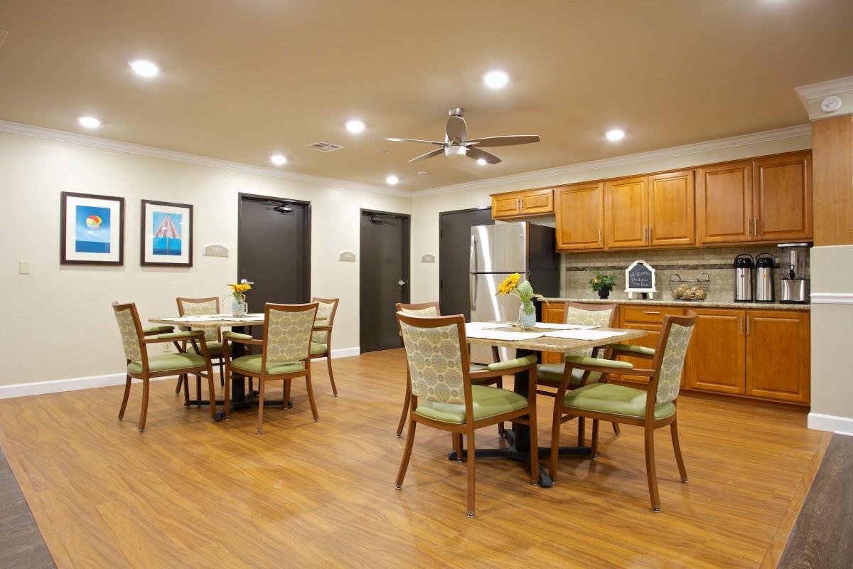 A modern dining area with multiple tables and chairs, adjacent to a kitchen with wooden cabinetry and stainless steel appliances.