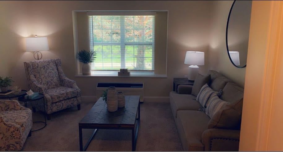 A cozy living room with a sofa, coffee table, and soft lighting from a lamp near the window.