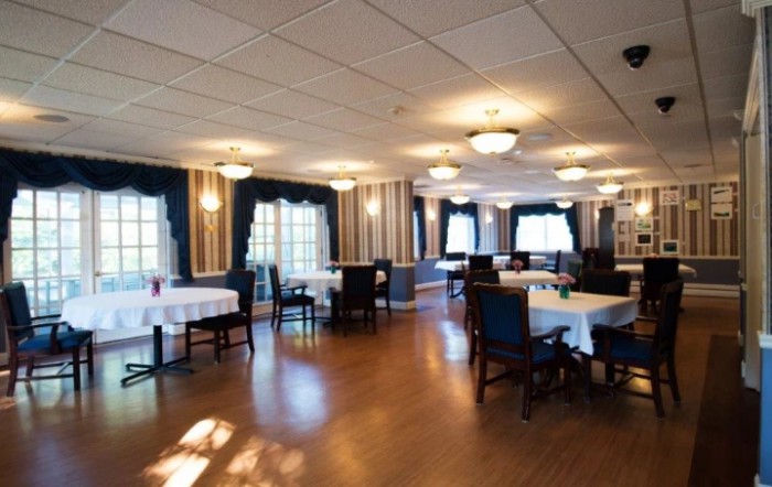 A spacious restaurant dining area with neatly arranged tables and chairs, well-lit by ceiling lights and natural light from the windows.