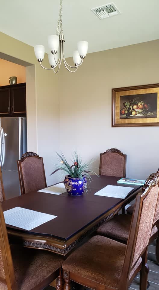 A cozy dining area with a wooden table, cushioned chairs, a plant centerpiece, and framed artwork on the wall.