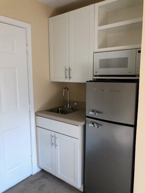 A compact kitchenette featuring a sink, cabinets, a microwave, and a refrigerator.