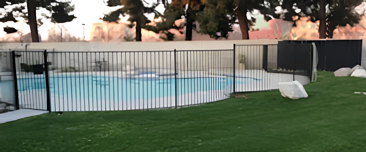 A fenced swimming pool surrounded by grass and trees.