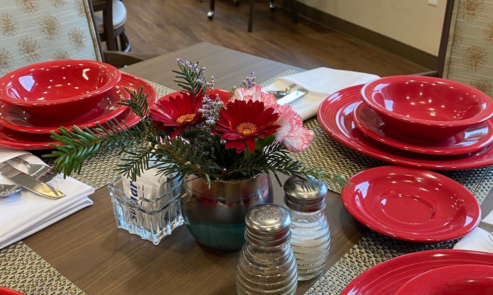 A dining table set with red plates and a floral centerpiece.