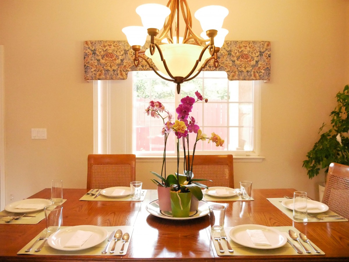 An elegantly set dining table with an orchid centerpiece and chandelier lighting.