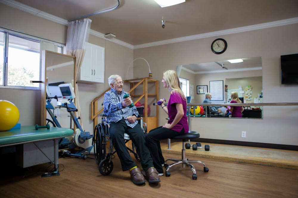 An elderly person sits in a wheelchair while engaging with a therapist in a rehabilitation clinic.