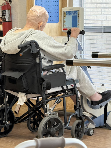 An elderly individual participating in rehabilitation, using a wheelchair during physical therapy.