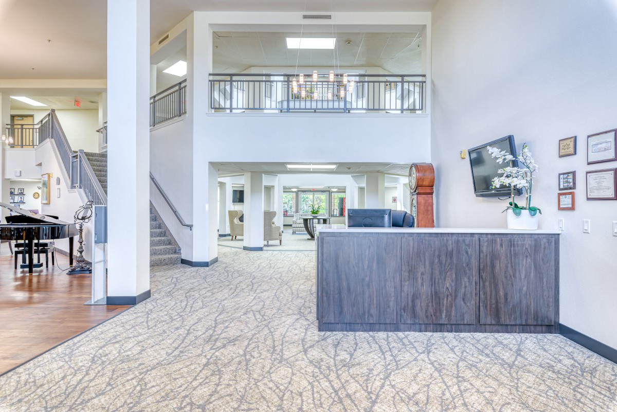 A modern and spacious lobby area featuring a reception desk, staircase, and balcony.