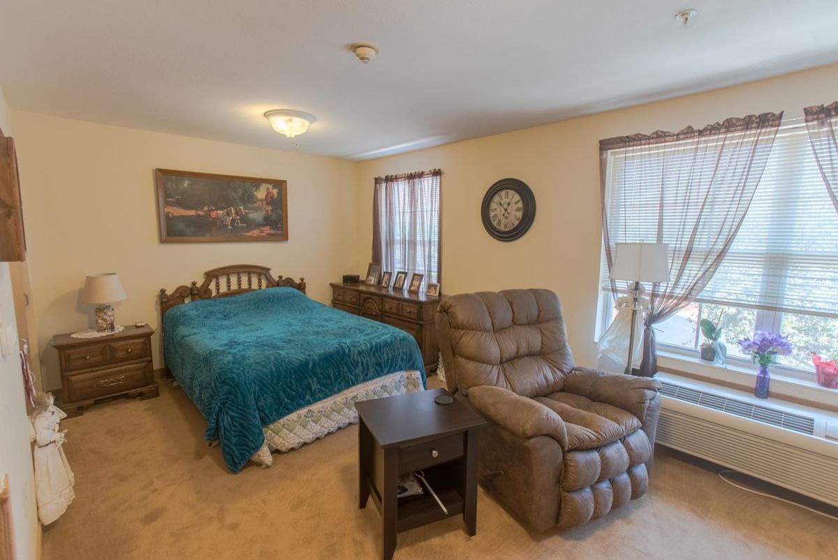 A cozy bedroom featuring a bed with a teal blanket, an armchair, and a window with curtains.