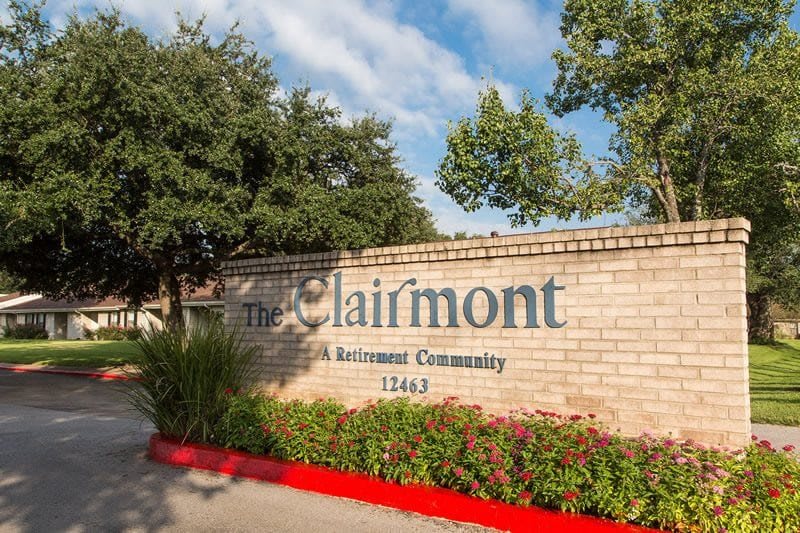 Entrance to The Clairmont Retirement Community with brick signage and surrounding greenery.