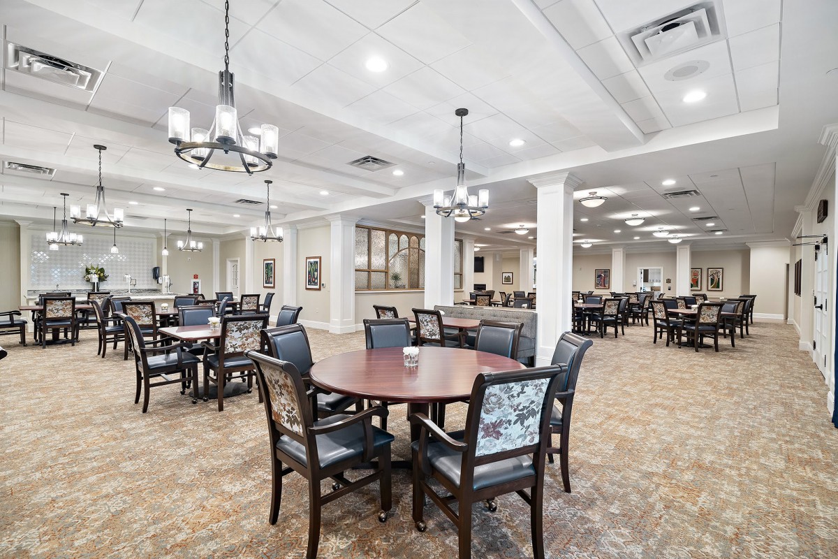 A spacious dining area with neatly arranged tables and chairs, illuminated by elegant chandeliers.