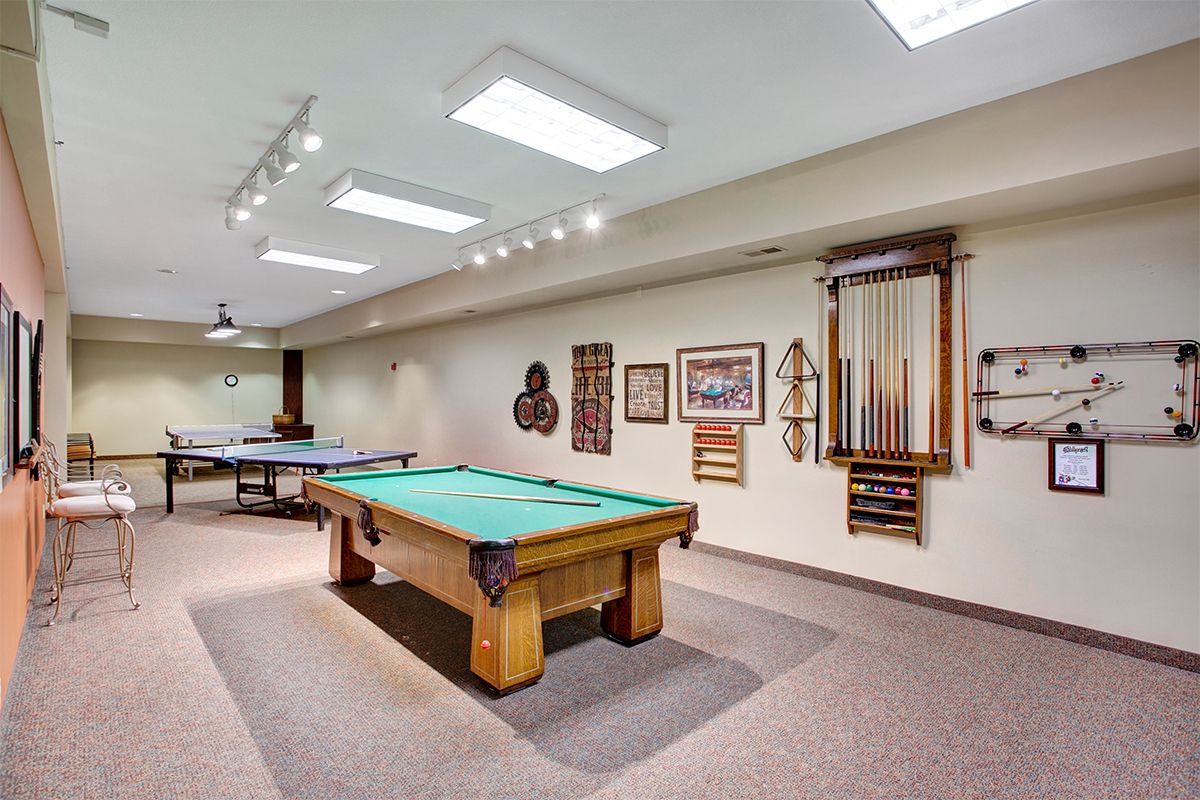 A well-designed billiards room featuring a green pool table, decorative wall art, and neatly arranged cue sticks.