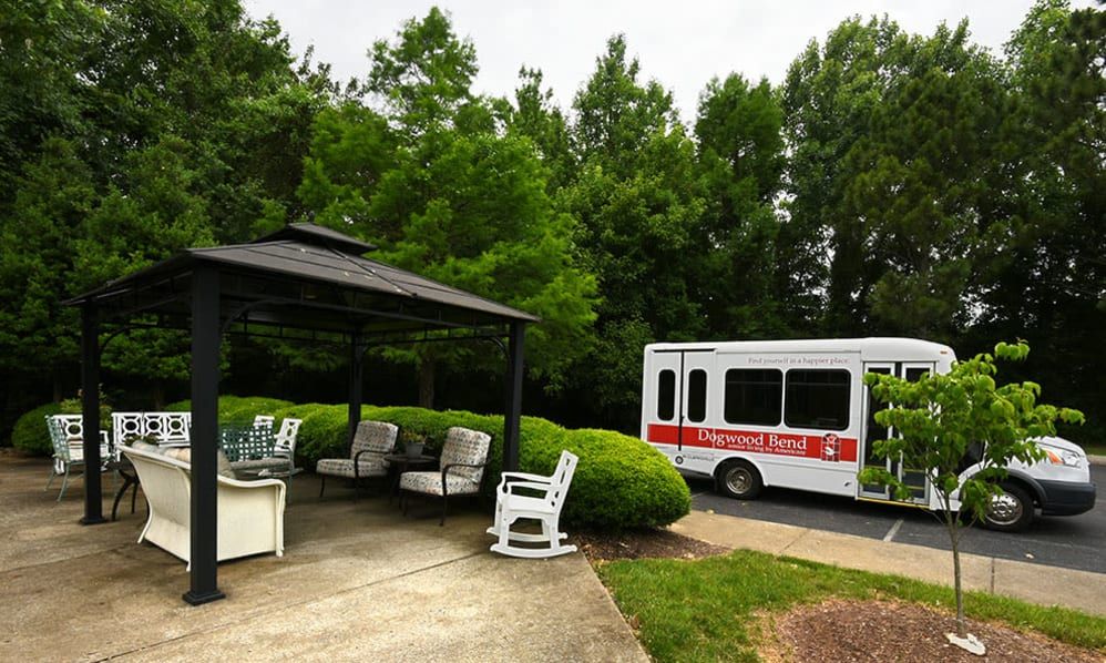 A peaceful outdoor area with a gazebo and seating near a parked bus, surrounded by lush greenery.