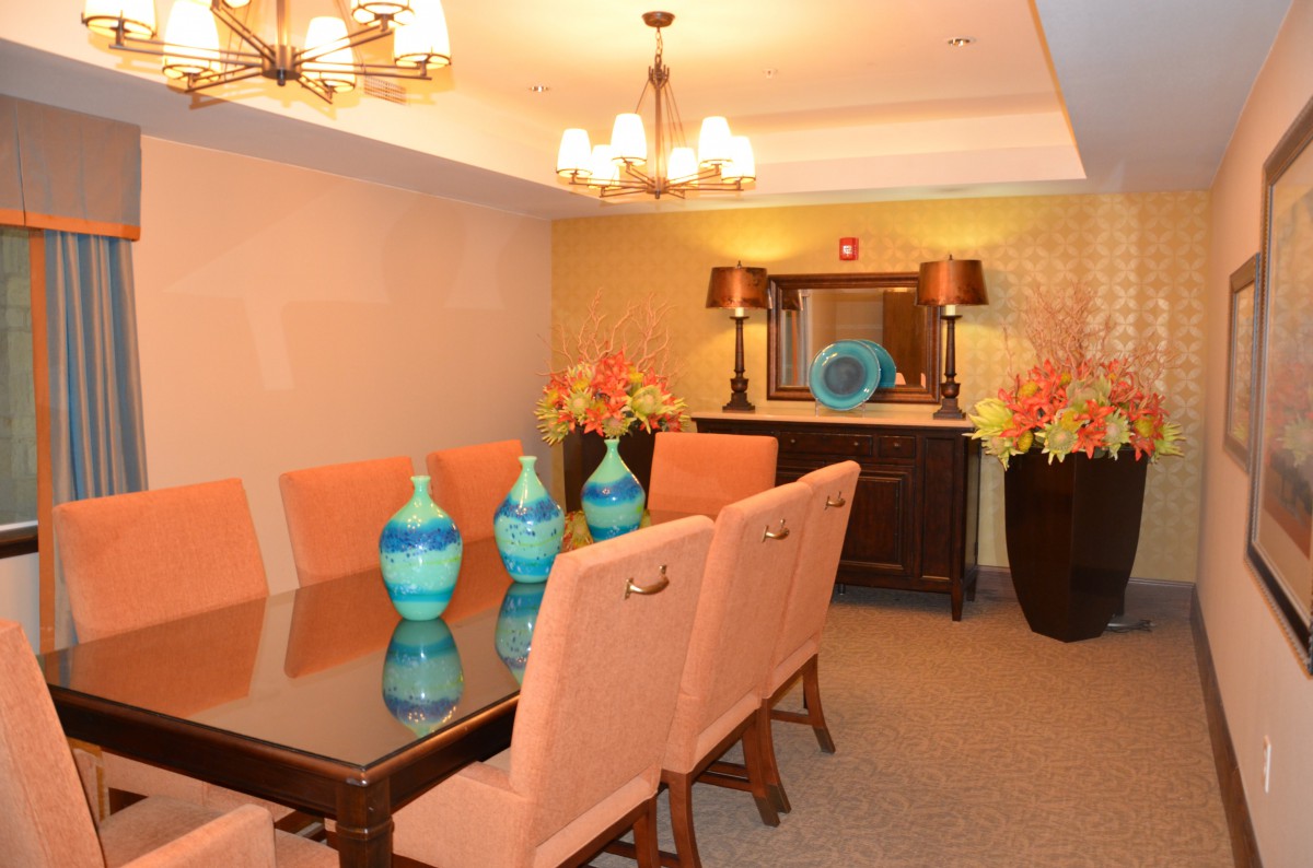 A stylish dining room featuring a glass-topped table with pink upholstered chairs, accentuated by vibrant blue vases and elegant lighting.