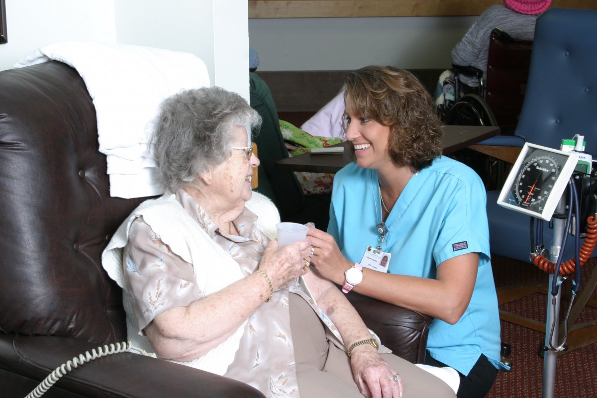 A healthcare professional interacts warmly with an elderly woman.