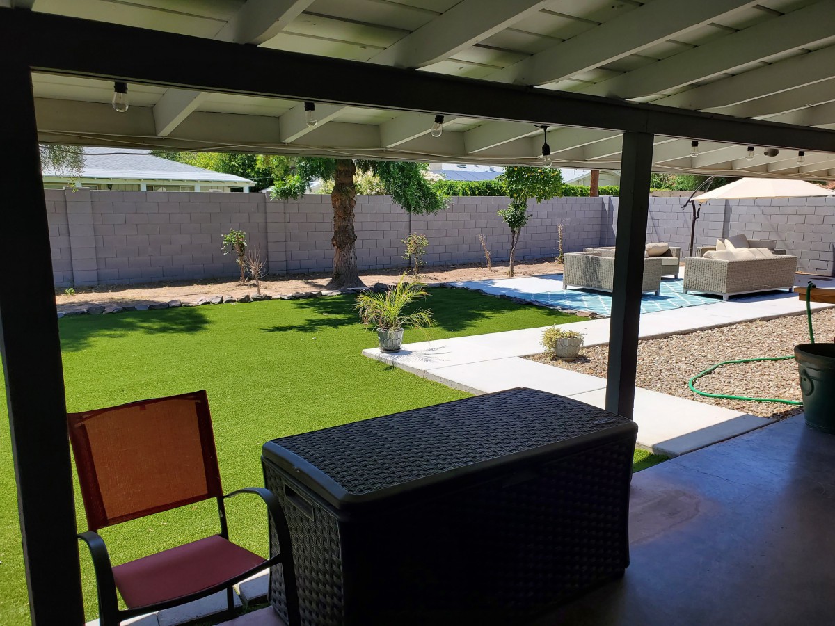 A serene backyard with a patio, lawn, and swimming pool under clear skies.