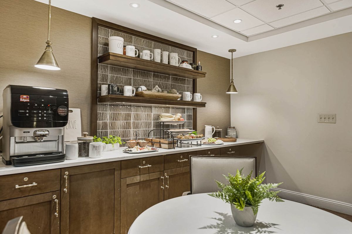 A modern kitchen space with a coffee station, shelves, and dining table.