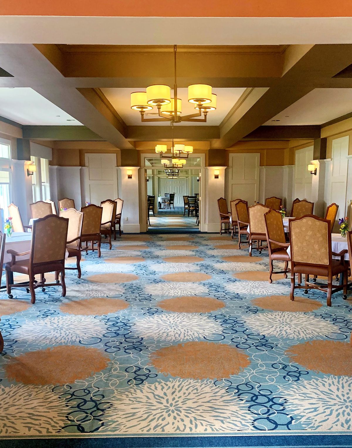 A spacious dining room with elegant chairs and tables, featuring a patterned carpet and ambient lighting.