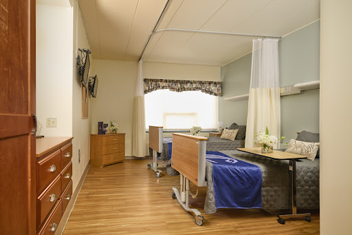 A well-designed hospital patient room featuring two beds, a television, and bright natural light.