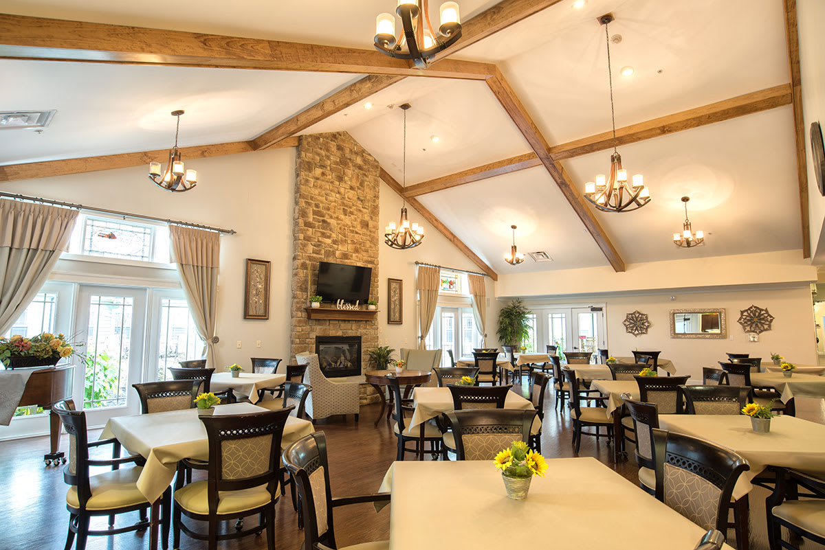 A spacious and well-lit dining area with wooden beams, a stone fireplace, and elegant chandeliers.