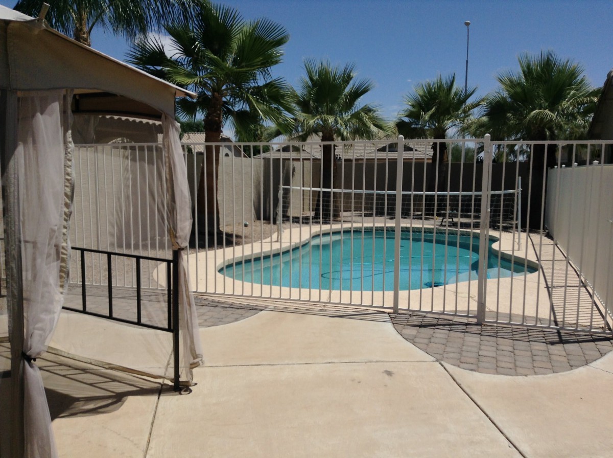 A fenced swimming pool area with palm trees under a clear blue sky.