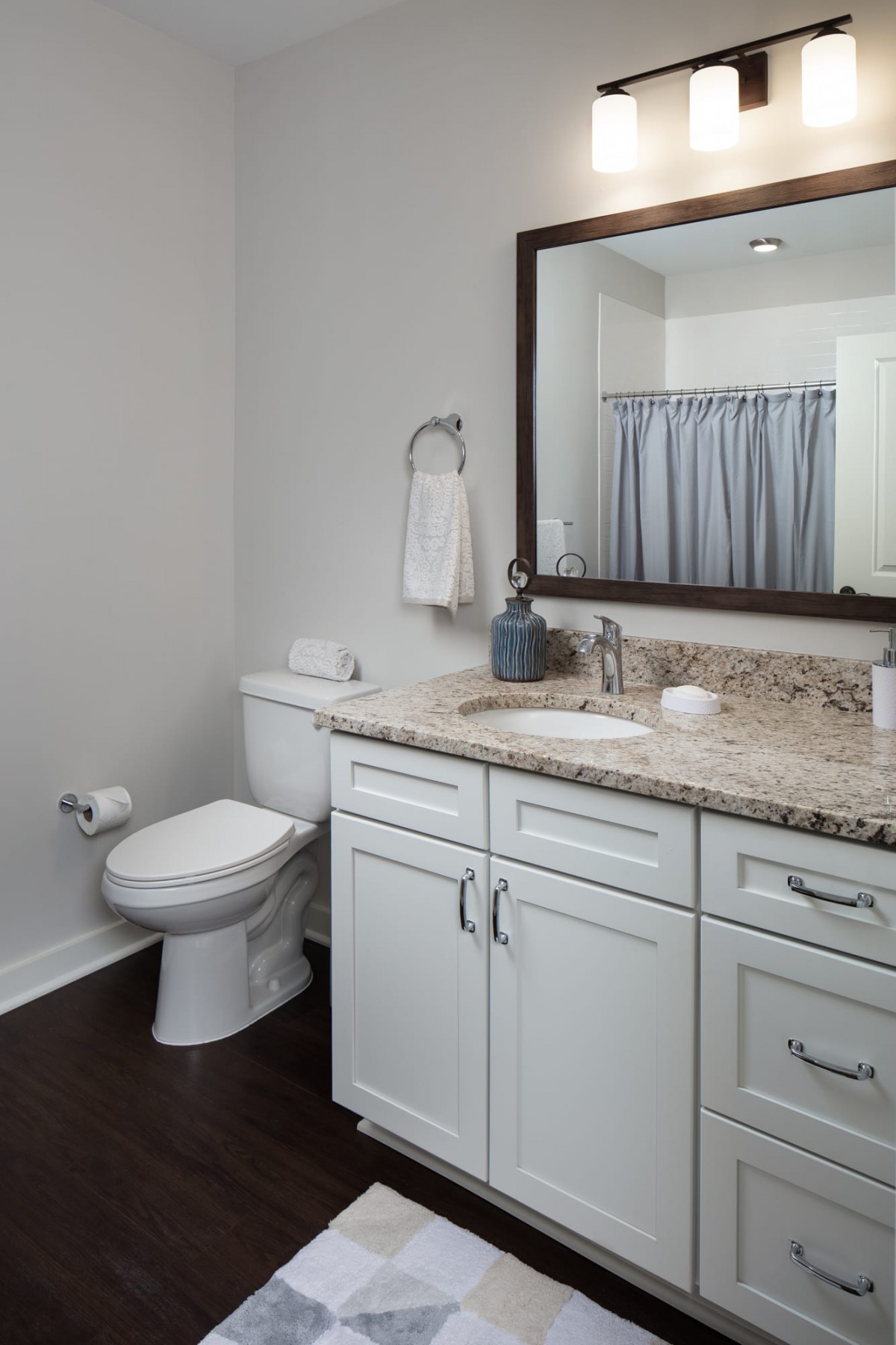 A well-organized bathroom with a granite countertop, white cabinets, and a shower curtain.