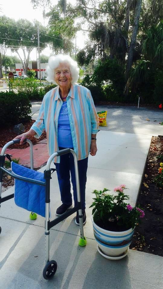 Elderly woman with a walker enjoying gardening outdoors.