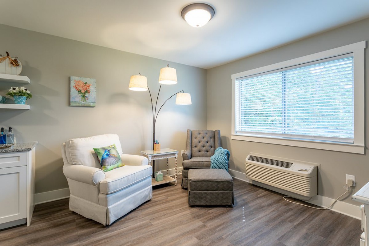 A cozy living room with comfortable armchairs, a floor lamp, and natural light streaming through the window.