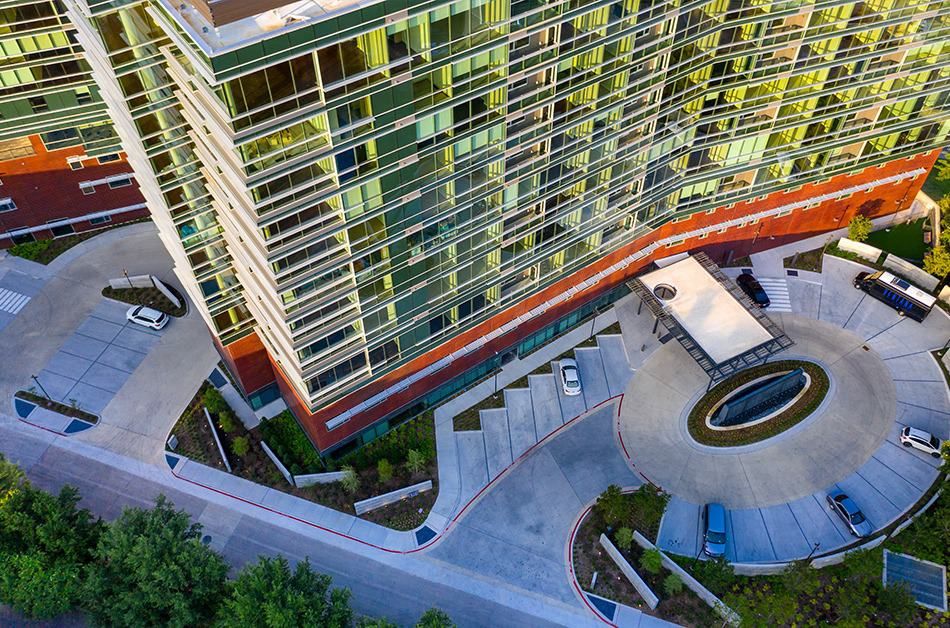 An aerial view of a modern, multi-story apartment building with a landscaped entrance.