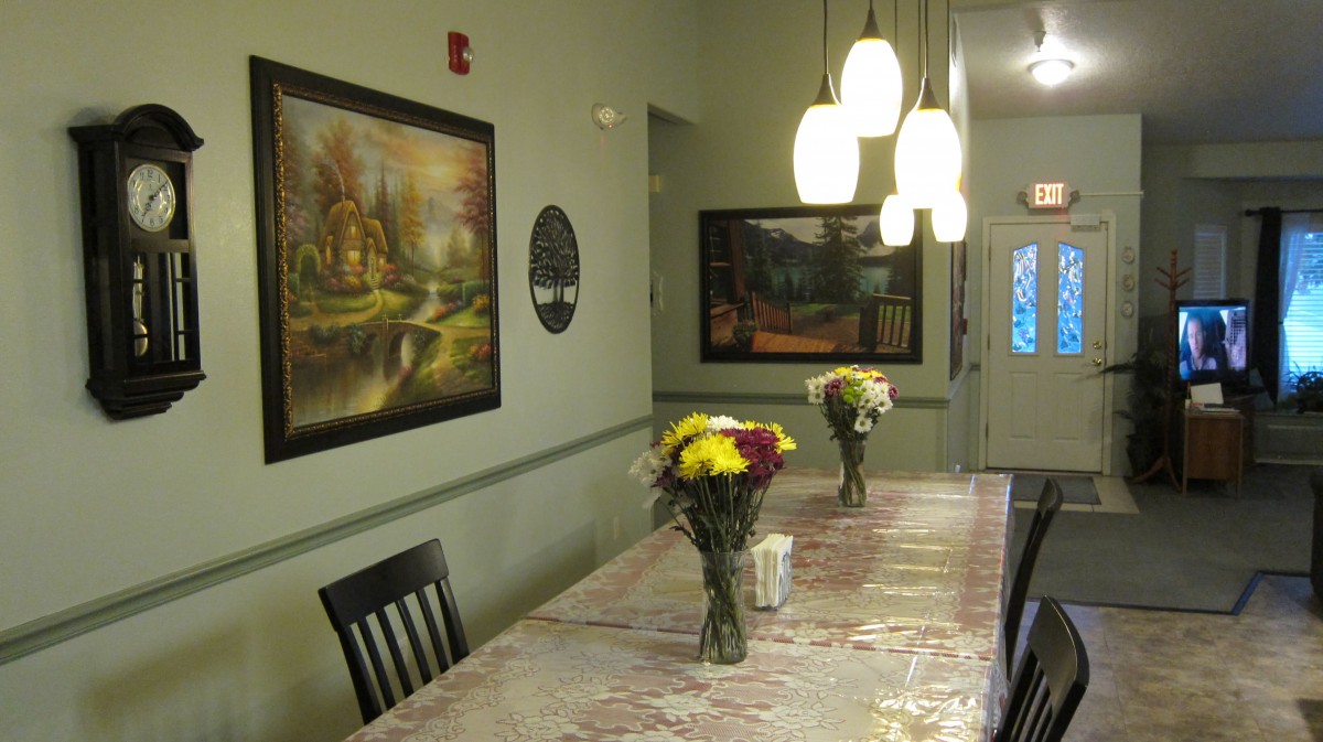 A cozy dining room with a decorated table, featuring fresh flower arrangements and illuminated by pendant lights.