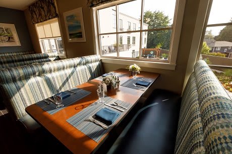 A cozy restaurant booth with a neatly set table and a sunny window view.