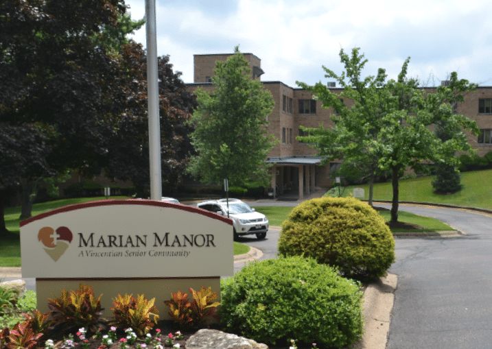 A scenic view of a building with surrounding greenery and a sign reading 'Marian Manor'.