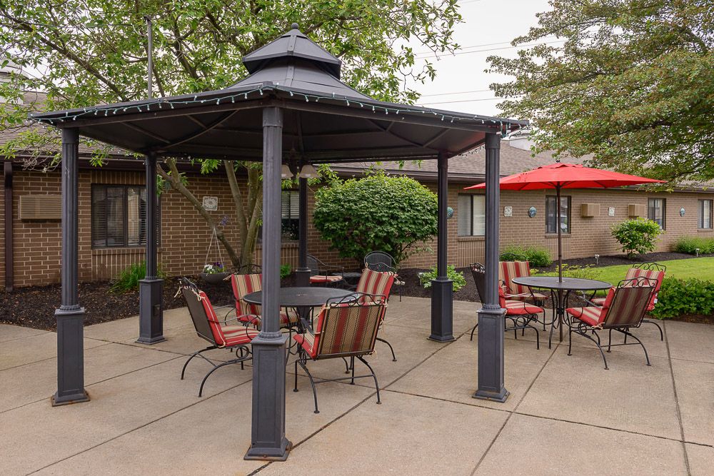 An outdoor patio area featuring a gazebo with chairs and a table, surrounded by trees and additional seating with umbrellas.