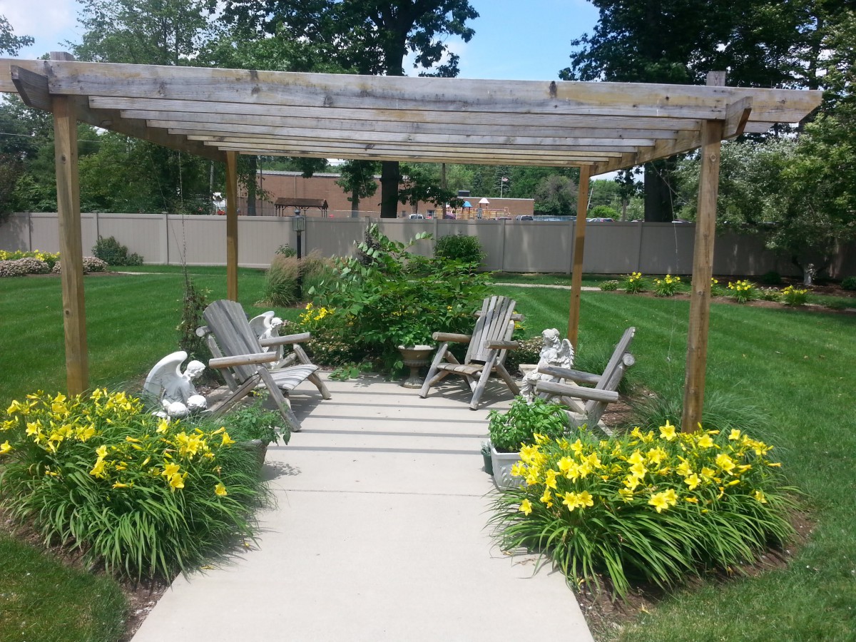 A peaceful garden scene with a pergola, surrounded by flowers and outdoor seating.