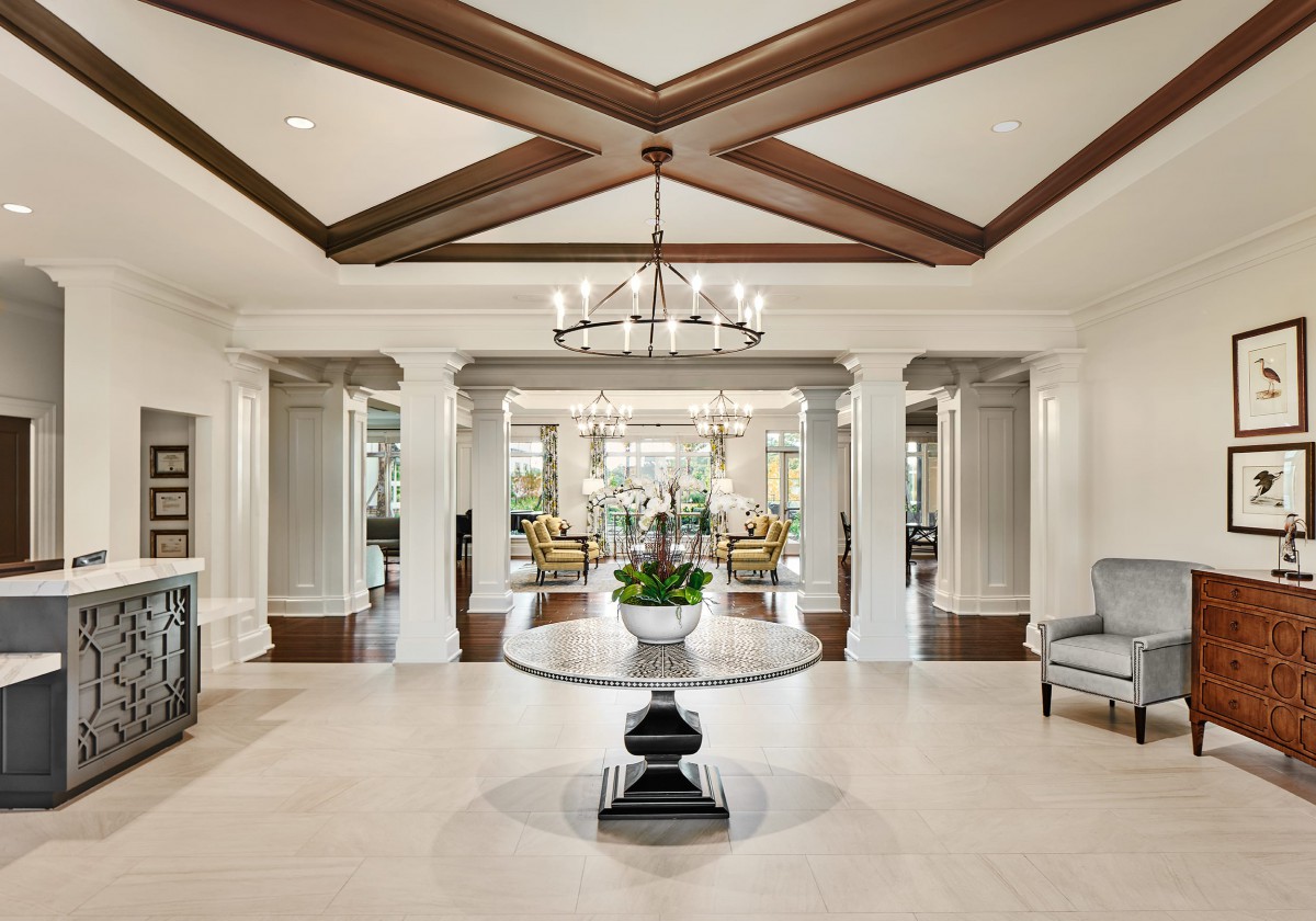 A luxurious foyer featuring a central round table, elegant chandelier, and classical columns.