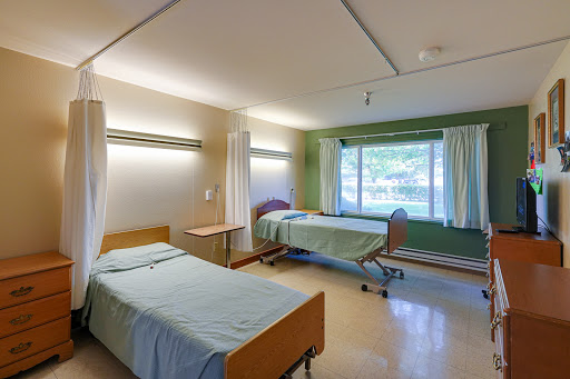 A spacious hospital patient room featuring two beds and natural light from a window.