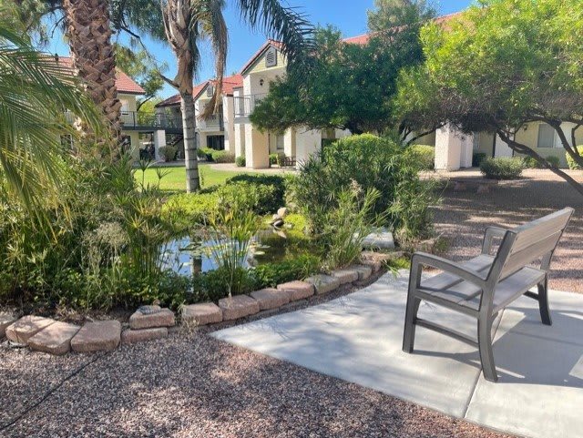 A serene outdoor garden with a pond, surrounded by lush greenery and a bench for relaxation.