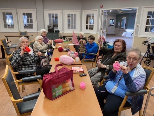 A group of elderly people enjoying a knitting session together indoors.