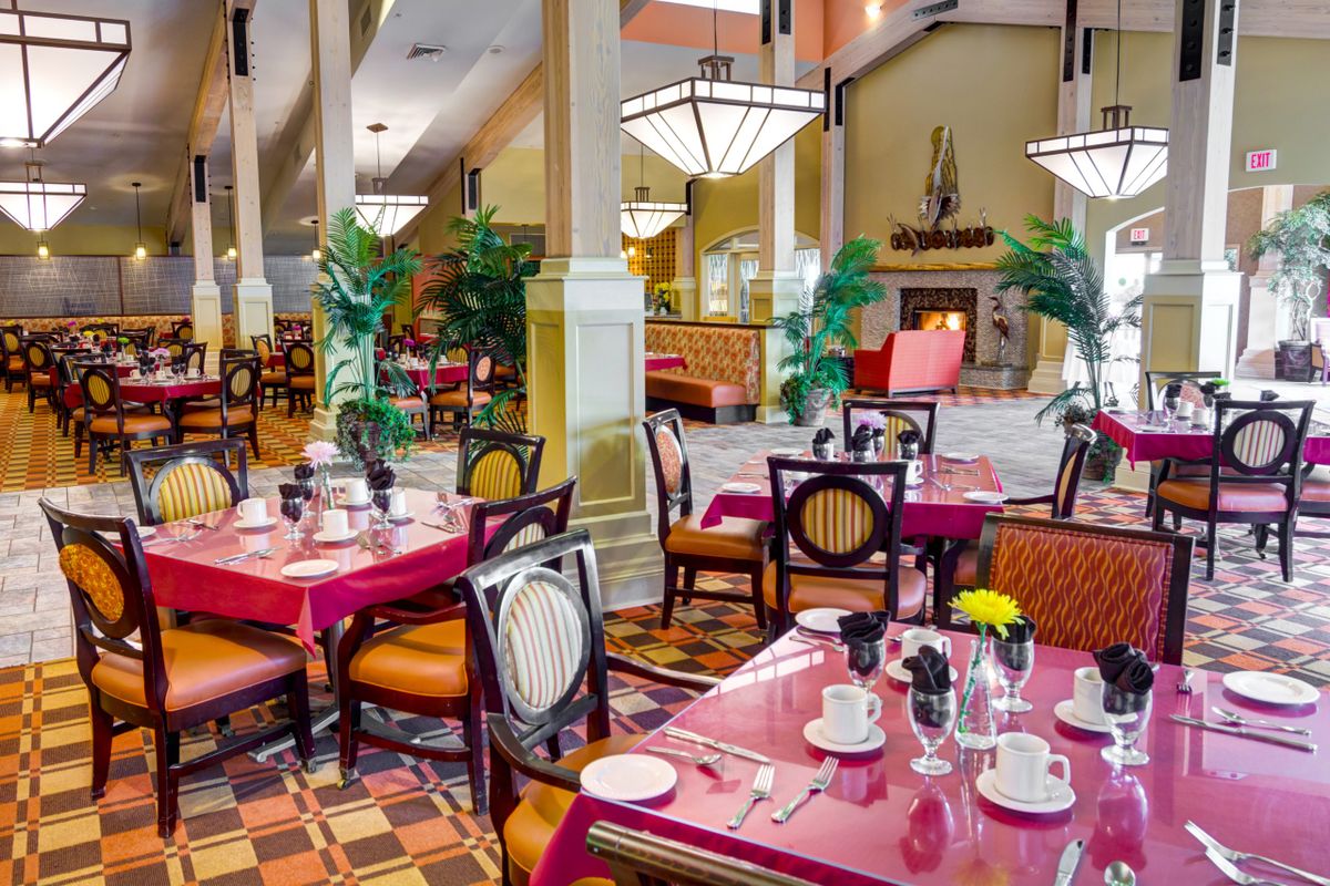 A beautifully decorated restaurant interior with neatly arranged tables and chairs, featuring elegant lighting and potted plants.