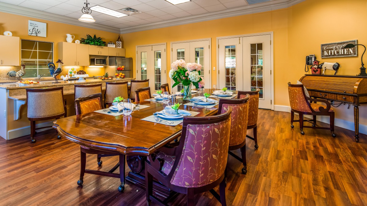 A warmly decorated dining room with a large wooden table, elegant chairs, and a floral centerpiece.