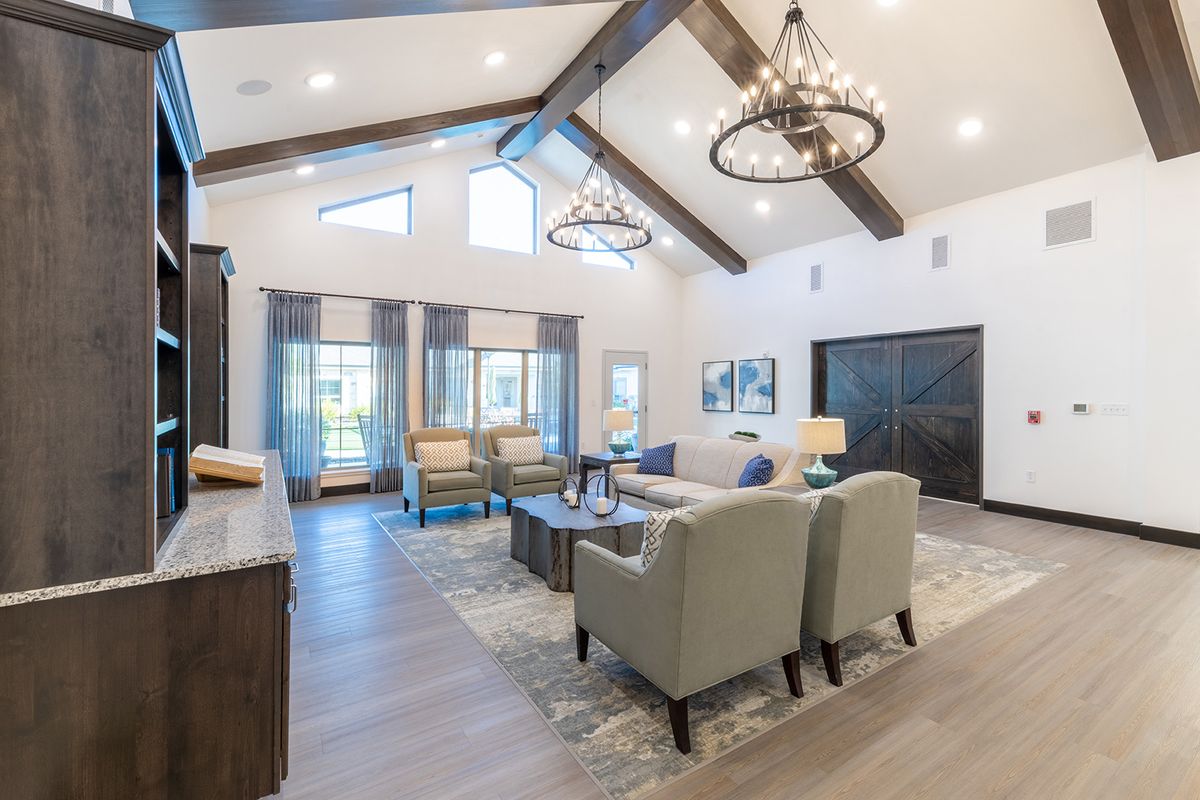 A modern living room with high ceilings, featuring elegant chandeliers, comfortable seating, and large windows that allow natural light to fill the space.