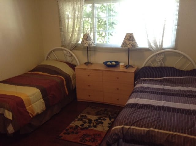 A cozy bedroom with two twin beds and a dresser between them, decorated with lamps and a window view.