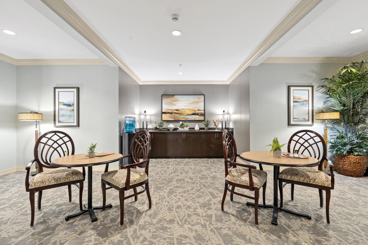 A neatly arranged seating area with tables and chairs, surrounded by elegant decor and paintings.