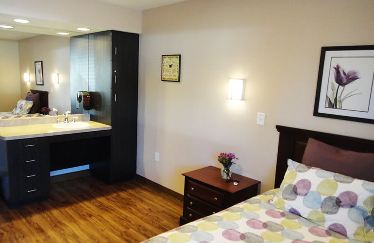 A cozy bedroom with a bed, side table, dresser, and wall-mounted lamp.
