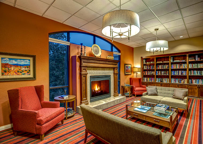 A cozy library with a fireplace, comfortable armchairs, and bookshelves filled with books.