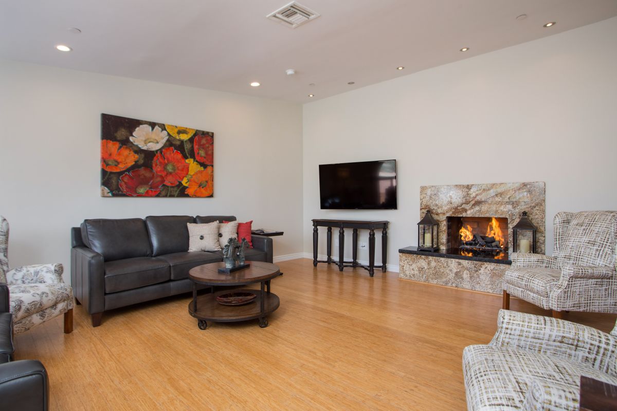 A cozy living room with a fireplace, featuring a gray sofa, wall-mounted TV, and colorful artwork.